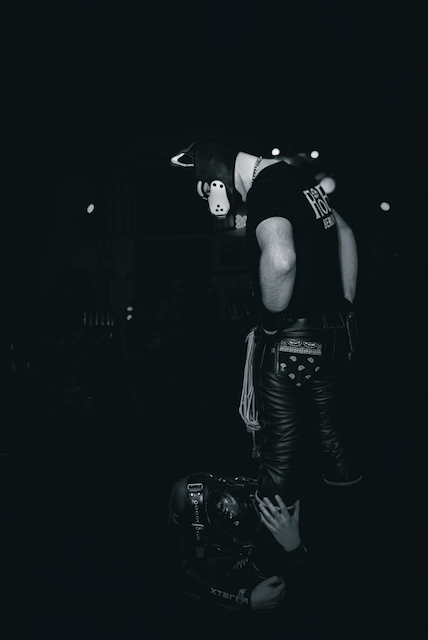 A leatherman standing over a kneeling partner